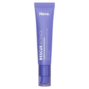 Na zdjęciu widoczny jest fioletowy, smukły tubkowy kosmetyk marki Hero Cosmetics o nazwie Rescue Retinol. Produkt opisany jest jako "Nighttime Renewing Cream" (krem odnawiający na noc) o pojemności 30 ml. Na opakowaniu wspomniano, że zawiera 0,75% enkapsulowanego retinolu oraz Rescue Balm Complex™, co sugeruje jego regeneracyjne i nawilżające właściwości. Tubka ma minimalistyczny design z białym tekstem na fioletowym tle i pompką ułatwiającą aplikację.