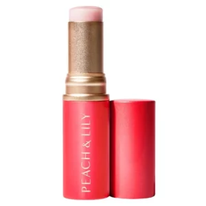 Zdjęcie przedstawia Peach & Lily Glass Skin Luminizing Stick, czyli rozświetlający balsam w sztyfcie. Produkt ma eleganckie, czerwone opakowanie ze złotymi akcentami i białym napisem „PEACH & LILY”. Po odkręceniu ukazuje się jasnoróżowy balsam o jedwabistej konsystencji. Sztyft jest przeznaczony do nadania skórze efektu Glass Skin, zapewniając subtelne rozświetlenie bez drobinek brokatu.