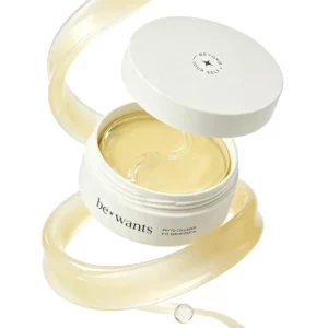 Otwarty biały słoiczek be+wants Phyto Collagen Eye Serum Patch ze złocistymi płatkami pod oczy, przedstawiony na jasnym tle z dekoracyjną smugą serum.