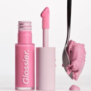 Produkt Glossier Lip Glaze w odcieniu Frosty: błyszczyk w różowej tubce z aplikatorem pokrytym jasnoróżowym produktem. Obok znajduje się łyżka z porcją różowych lodów, nawiązująca do odcienia błyszczyka.