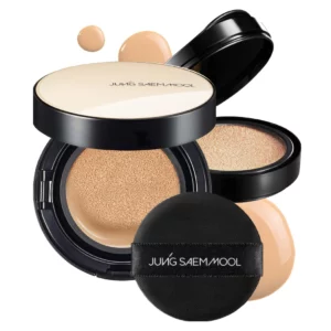 Otwarty kompaktowy cushion Jung Saem Mool Essential Skin Nuder Cushion SPF 50+ w odcieniu beżowym, pokazujący gąbeczkę nasączoną podkładem. W tle znajduje się czarna gąbka aplikacyjna z logo marki oraz rozlane krople produktu.