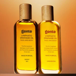 Dwie wersje olejku Gente Lymphatic Drainage Oil – pachnąca i bezzapachowa – stojące obok siebie na tle pomarańczowego gradientu.
