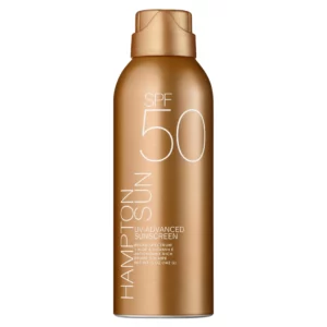 Na zdjęciu widoczna jest złoto-brązowa butelka aerozolu z filtrem przeciwsłonecznym Hampton Sun SPF 50. Produkt ma elegancki, matowy design z białym minimalistycznym napisem. Na froncie widnieją informacje o wysokiej ochronie przeciwsłonecznej (SPF 50), nazwie marki, a także wzmianka o zawartości aloesu i witaminy E.