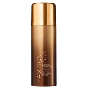 Zdjęcie przedstawia elegancki, brązowo-złoty aerozol Hampton Sun Sunless Tanning Mist o pojemności 142 g (5 oz). Na przedzie opakowania widnieje nazwa produktu oraz informacje: "No-Rub", "Quick-Drying", "Streak-Free", "Natural Color", wskazujące na jego właściwości – szybkoschnącą formułę, brak konieczności wcierania i naturalny efekt opalenizny bez smug.
