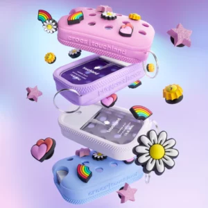 Zawieszone w powietrzu cztery opakowania Touchland Power Mist w stylizowanych, kolorowych etui przypominających Crocs, z przypinkami w kształcie stokrotek, serc, gwiazd i tęczy. Obraz dynamiczny, z elementami unoszącymi się w pastelowym tle.