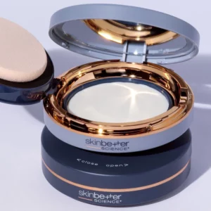 Otwarte pudełeczko kremu z filtrem spf Skinbetter Sheer Sunscreen Compact, na jasnofioletowym tle.