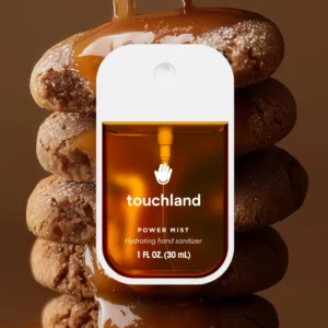 Hydrating hand sanitizer Touchland Power Mist w wariancie Cinnamon Gingerbread, zaprezentowany na tle stosu pierniczków oblanych karmelem.