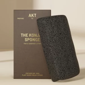 Czarno-brązowe pudełko z napisem „AKT The Konjac Sponge” oraz czarna gąbka konjac oparta o opakowanie.