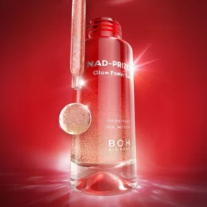 Butelka serum Bioheal Boh NAD-Prizcell Glow Power Serum w czerwonym szkle z pipetą i kroplą produktu na tle czerwonego światła.