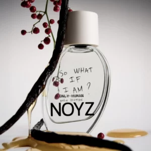 Flakon NOYZ Only Human w ciepłej, złocistej tonacji zdjęcia, otoczony ciemnymi, skręconymi laskami wanilii, w klimatycznej, artystycznej kompozycji.