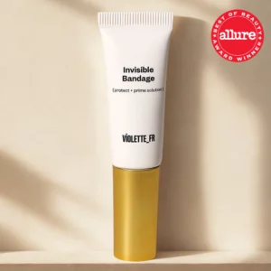 Tubka produktu Invisible Bandage (protect + prime solution) marki Violette_FR w białym opakowaniu ze złotą zakrętką, ustawiona na jasnym, beżowym tle z miękkim światłem i cieniem. W prawym górnym rogu widoczny czerwony znak „Allure Best of Beauty Award Winner”.
