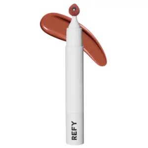 Biały aplikator do ust REFY Lip Sculpt z miękką, gąbkową końcówką w odcieniu ciepłego brązu, przedstawiony na tle smugi pomadki w tym samym kolorze, symbolizujący intensywny i kremowy pigment produktu.