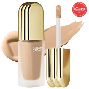 Korektor Sarah Creal Face Flex Concealer & Complexion Enhancer z aplikatorem i swatchem odcienia za produktem - wysoka jakość krycia i rozświetlające wykończenie. W górnym rogu widoczne logo nagrody.