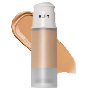 Na zdjęciu widoczny jest produkt REFY Skin Base w opakowaniu typu airless z rozprowadzoną obok formułą. Kremowa konsystencja sugeruje lekkie krycie i naturalne wykończenie na skórze.