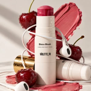 Violette_FR Bisou Blush - kremowy róż do policzków w sztyfcie z wbudowanym pędzlem, pokazany w soczystej aranżacji z wiśniami, różowo-koralową teksturą kosmetyku i białymi słuchawkami.