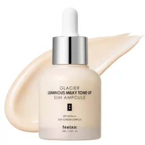 Packshot produktu Feelxo Glacier Luminous Milky Tone Up Sun Ampoule na jasnym tle z dekoracyjną smugą kremowej formuły za butelką. Minimalistyczna estetyka podkreśla lekki, rozświetlający charakter produktu SPF.