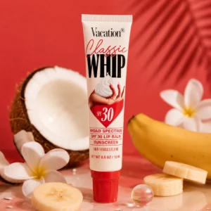 Vacation Classic Whip Lip Balm SPF 30 w otoczeniu kokosa, banana i białych kwiatów na czerwonym tle. Grafika podkreśla kokosowo-waniliowy smak balsamu oraz wakacyjny klimat produktu.