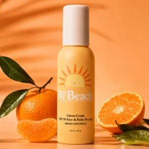 By The Beach Citrus Crush SPF 30 Face & Body Dry Oil – suchy olejek przeciwsłoneczny do twarzy i ciała z ochroną UVA i UVB na tle świeżych mandarynek i zielonych liści.