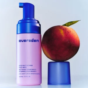 Evereden Kids Multi-Vitamin Face Wash w różowym opakowaniu z pompką obok soczystej brzoskwini, nawiązującej do świeżego zapachu Cool Peach.