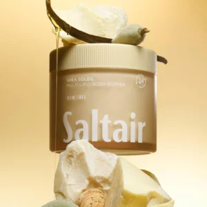 Saltair Shea Soleil Multi-Lipid Body Butter w stylizowanej kompozycji z masłem shea, laską wanilii, migdałem i złocistym tłem.