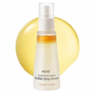 Packshot su:m37 Secret Pore Ceramide Bubble Spray Serum na jasnym tle. Przed butelką widoczna jest złocista kropla symbolizująca trójwarstwową formułę zawierającą olejek, kapsułki pielęgnacyjne i esencję.