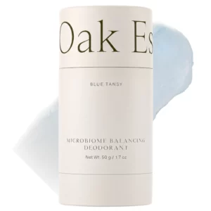 Oak Essentials Blue Tansy Microbiome Balancing Deodorant w beżowym opakowaniu z jasnoniebieską teksturą produktu w tle.