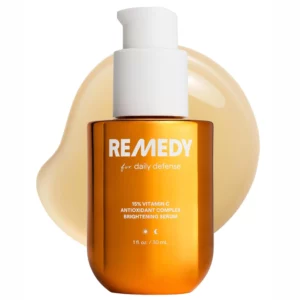 Bursztynowa butelka serum Remedy 15% Vitamin C Complex Brightening Serum z białą pompką na jasnym tle i złotą kroplą konsystencji.