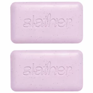 Dwie jasnoróżowe kostki Topicals Slather Exfoliating & Smoothing Bar z wytłoczonym logo, ułożone jedna nad drugą na białym tle.