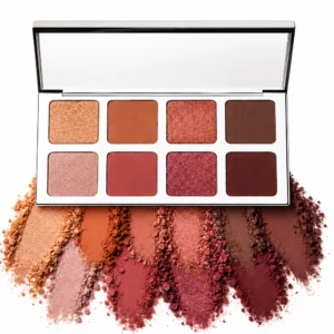 Na zdjęciu znajduje się otwarta paleta cieni IL Makiage Color Boss Master Eyeshadow Palette z ośmioma odcieniami nude, różu, brązu i burgundu oraz rozsypanymi pigmentami w dopasowanych kolorach na białym tle.