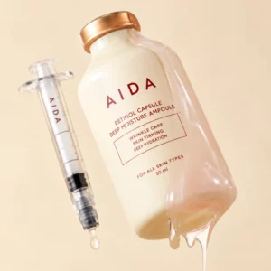 AIDA Retinol Capsule Deep Moisture Ampoule - ampułka z retinolem w eleganckiej fiolce ze złotym zamknięciem, przedstawiona obok aplikatora w formie strzykawki na kremowym tle.