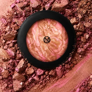 IL MAKIAGE Mineral Baked Bronzer w odcieniu Touch Me - marmurkowy bronzer w różowo-brązowo-złotych tonach, w czarnym okrągłym opakowaniu, otoczony rozkruszonym i rozsypanym pigmentem.