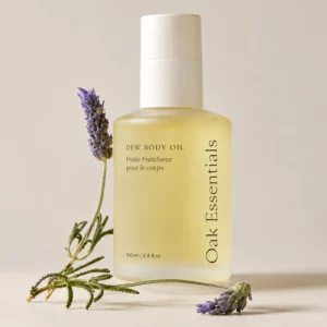 Start 47 Oak Essentials Dew Body Oil 100 ml - olejek do ciała w eleganckiej szklanej butelce, przedstawiony z gałązkami lawendy na beżowym tle.
