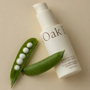 Start 82 Oak Essentials Firming Plant Peptide Serum 30 ml - peptydowe serum do twarzy w kremowej butelce z pompką, przedstawione z zielonymi strąkami grochu na beżowym tle.