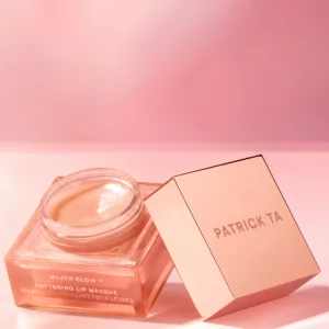 Start 60 Patrick Ta Major Glow Softening Lip Masque - luksusowa, nawilżająca maska do ust o bogatej, kremowej konsystencji i subtelnym połysku. Otwarty słoiczek w brzoskwiniowo-różowym odcieniu z elegancką pokrywką w kolorze różowego złota, na pastelowym różowym tle. Kosmetyk pomaga odżywić, wygładzić i zmiękczyć usta, nadając im zdrowy, promienny wygląd.