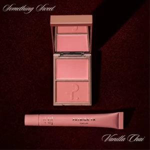Start 109 Patrick Ta Major Headlines Blush & Lip Balm Set Something Sweet + Vanilla Chai - otwarty kremowo-pudrowy róż w delikatnym różowym odcieniu oraz balsam do ust Vanilla Chai na bordowym, połyskującym tle.