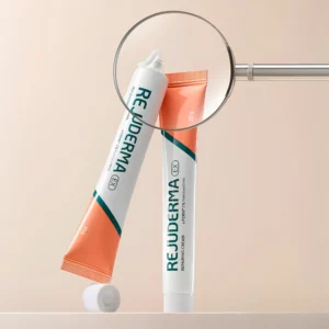 Start 7 REJUDERMA EX Repairing Cream c-PDRN 1% - koreański krem kojąco-odbudowujący do twarzy, dwie biało-koralowe tubki 20 g z zielonym logo marki, jedna otwarta z widoczną konsystencją kremu, elegancka kompozycja z lupą na beżowym tle.